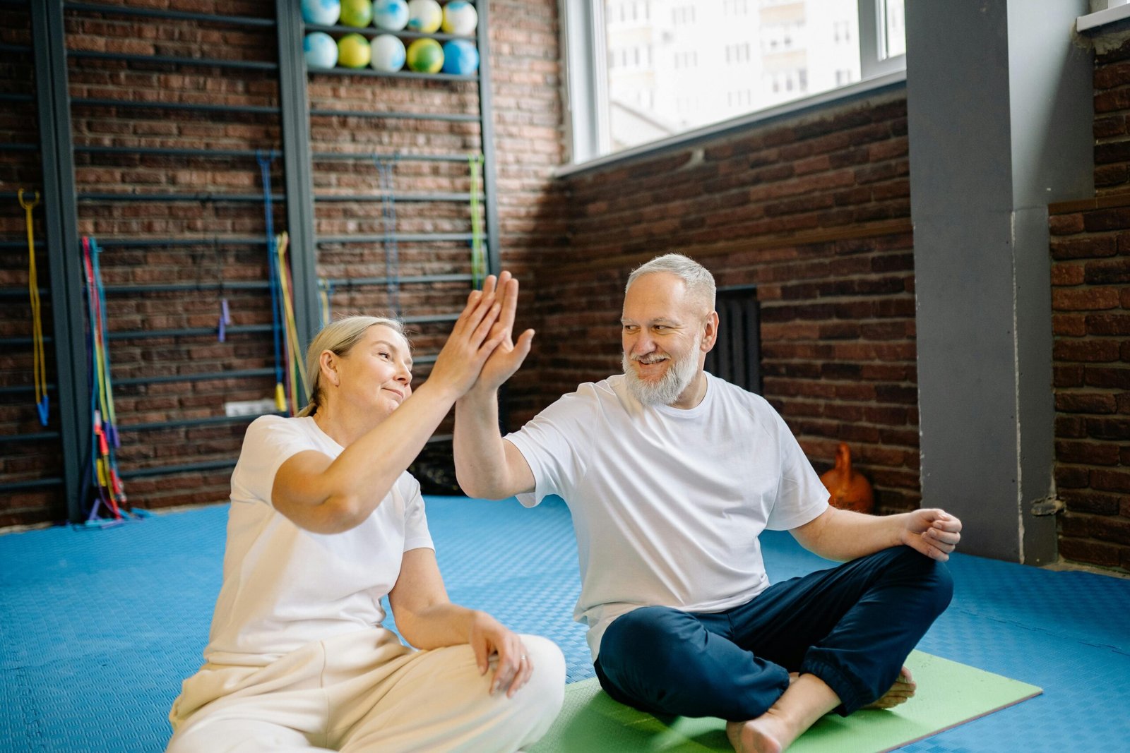 Energetic senior couple enjoying yoga, sharing a joyful high-five at the gym.